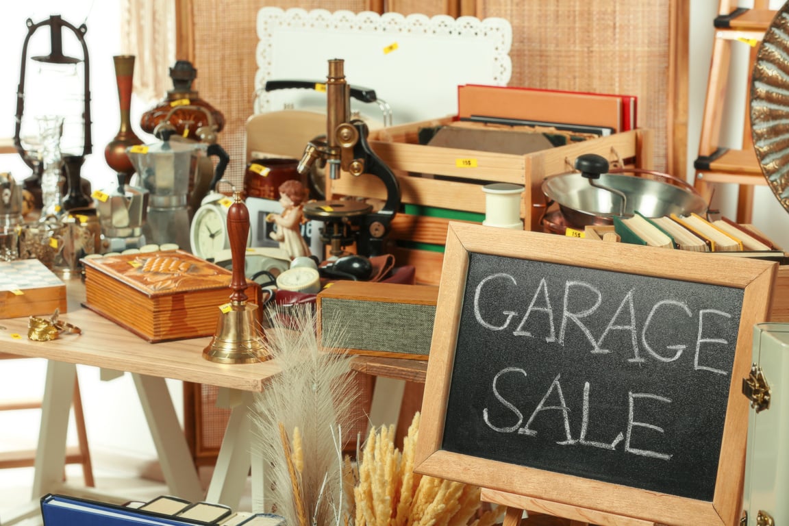 Sign Garage Sale Written on Blackboard near Many Different Stuff